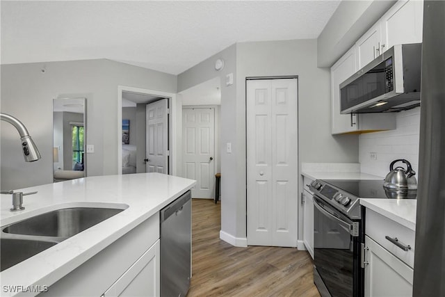 kitchen featuring tasteful backsplash, white cabinetry, sink, stainless steel appliances, and light hardwood / wood-style flooring