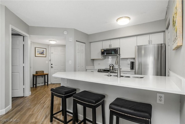 kitchen featuring appliances with stainless steel finishes, a breakfast bar, white cabinetry, sink, and kitchen peninsula