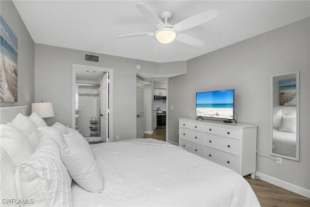 bedroom with ceiling fan, connected bathroom, a textured ceiling, and dark hardwood / wood-style flooring