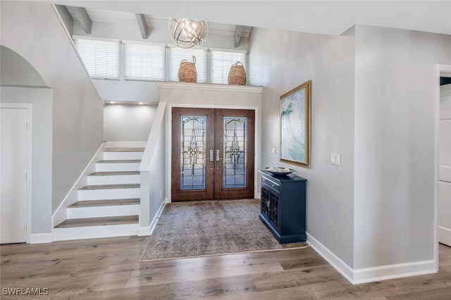 foyer with hardwood / wood-style flooring, beam ceiling, an inviting chandelier, and french doors