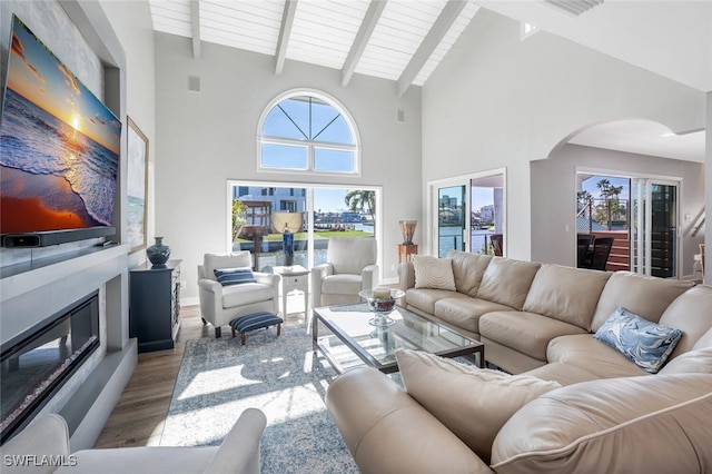 living area featuring visible vents, arched walkways, a glass covered fireplace, beamed ceiling, and light wood-type flooring