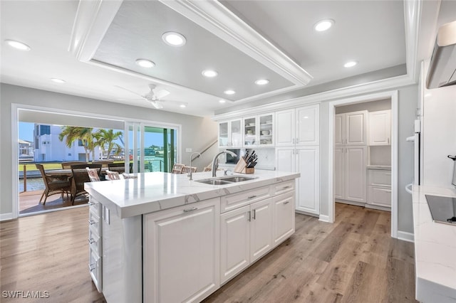 kitchen featuring a center island with sink, light wood-style flooring, glass insert cabinets, white cabinetry, and a sink