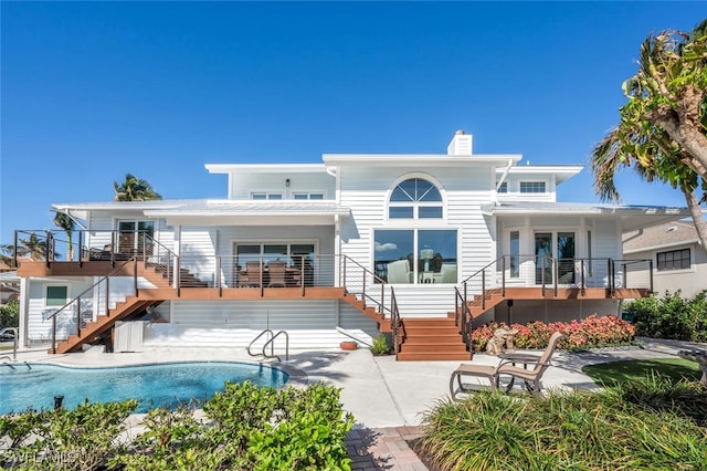 back of property with a chimney, stairway, an outdoor pool, and a patio