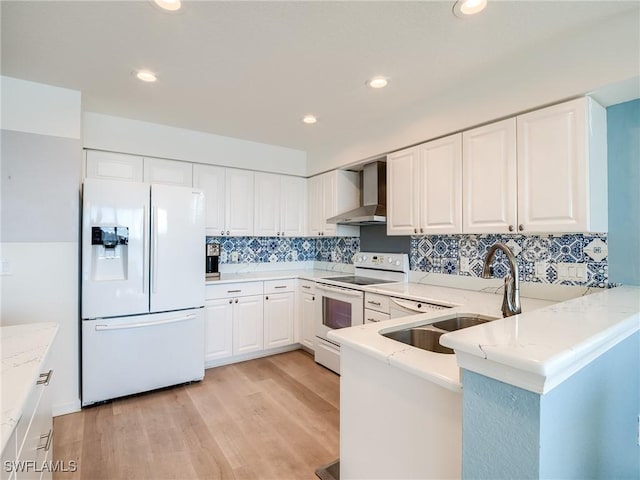 kitchen featuring wall chimney exhaust hood, white cabinetry, white appliances, and kitchen peninsula