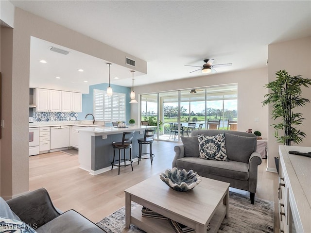 living room with ceiling fan, sink, and light wood-type flooring