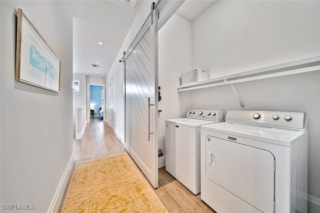 laundry room with a barn door, light hardwood / wood-style floors, and independent washer and dryer