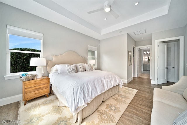 bedroom with hardwood / wood-style floors, ceiling fan, ensuite bath, and a tray ceiling