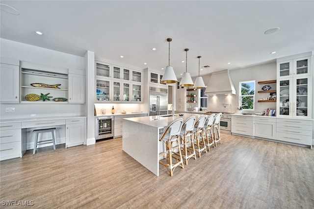 kitchen with a spacious island, custom exhaust hood, high quality appliances, white cabinetry, and wine cooler