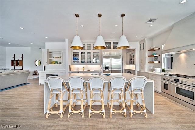 kitchen with high end appliances, light wood-type flooring, hanging light fixtures, and a center island with sink