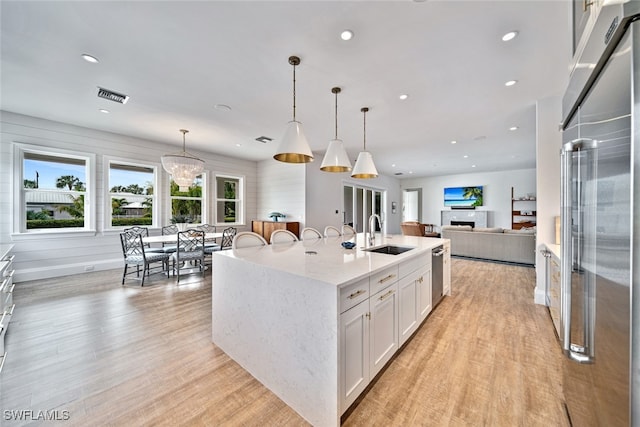 kitchen featuring white cabinetry, sink, decorative light fixtures, a kitchen island with sink, and high end fridge