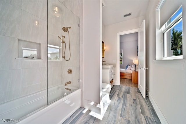 bathroom featuring toilet, a wealth of natural light, and shower / bath combination with glass door