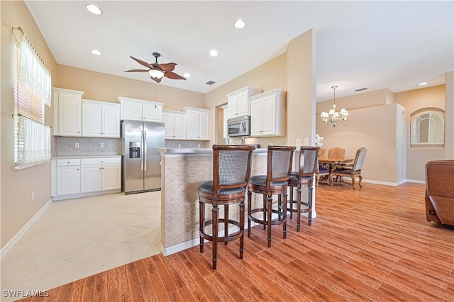 kitchen with appliances with stainless steel finishes, a breakfast bar, ceiling fan with notable chandelier, white cabinetry, and backsplash