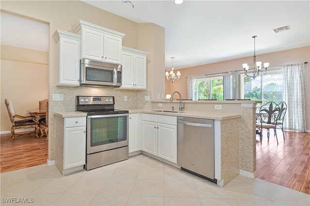 kitchen with white cabinets, stainless steel appliances, sink, and a notable chandelier