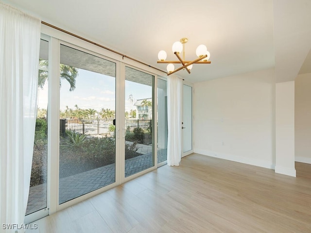 spare room with a healthy amount of sunlight, a chandelier, and light wood-type flooring