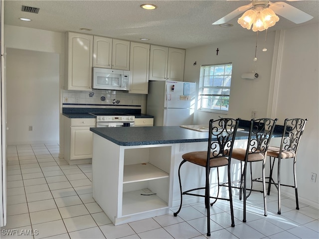 kitchen featuring light tile patterned flooring, white cabinetry, a textured ceiling, white appliances, and decorative backsplash