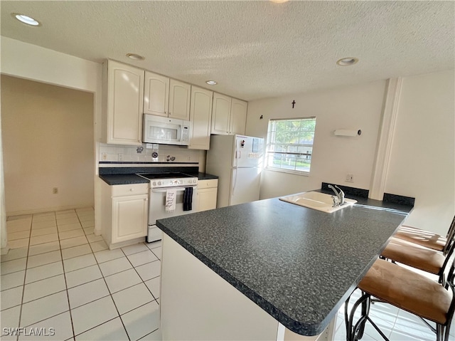 kitchen with white cabinets, kitchen peninsula, sink, a kitchen breakfast bar, and white appliances