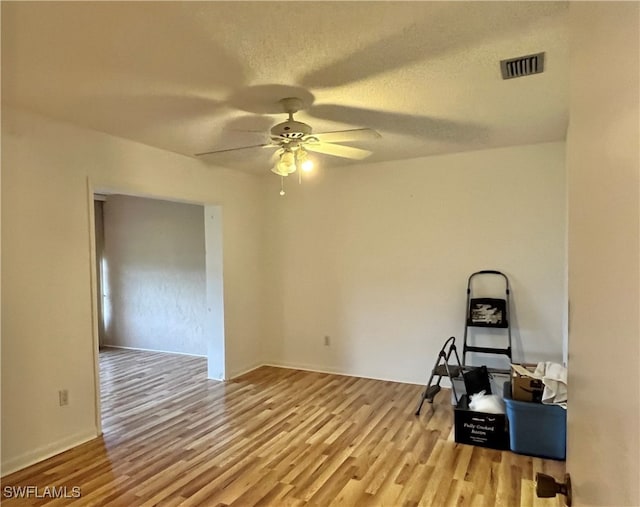 empty room featuring a textured ceiling, light wood-type flooring, and ceiling fan