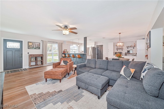 living room featuring ceiling fan with notable chandelier and light wood-type flooring