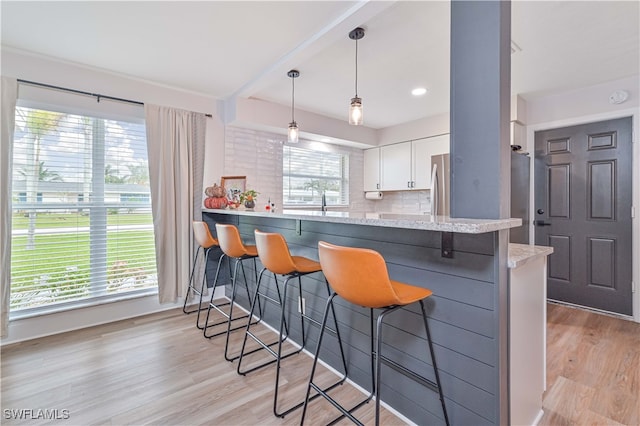 kitchen featuring pendant lighting, kitchen peninsula, a kitchen breakfast bar, backsplash, and white cabinetry