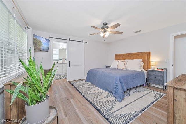 bedroom featuring light hardwood / wood-style floors, a barn door, and ceiling fan