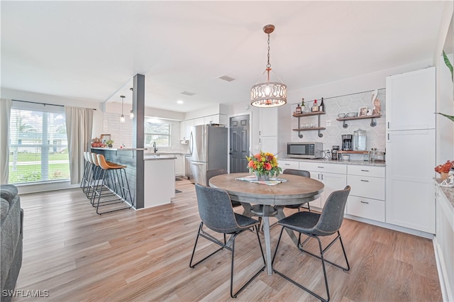 dining room featuring light wood-type flooring, a chandelier, sink, and plenty of natural light