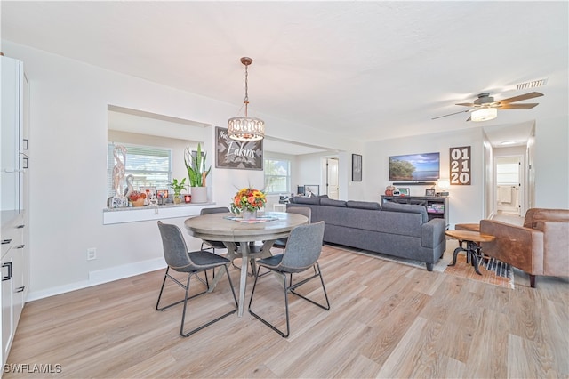 dining area with ceiling fan with notable chandelier and light hardwood / wood-style flooring