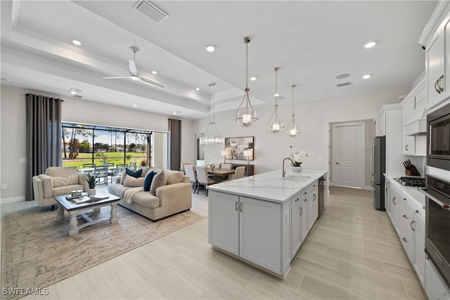 kitchen featuring light stone countertops, a kitchen island with sink, ceiling fan, decorative light fixtures, and white cabinets