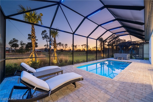 pool at dusk featuring glass enclosure, a hot tub, and a patio area