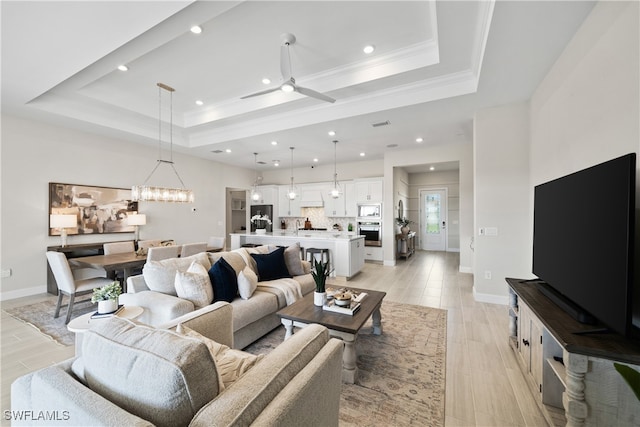 living room featuring a tray ceiling, crown molding, and ceiling fan with notable chandelier