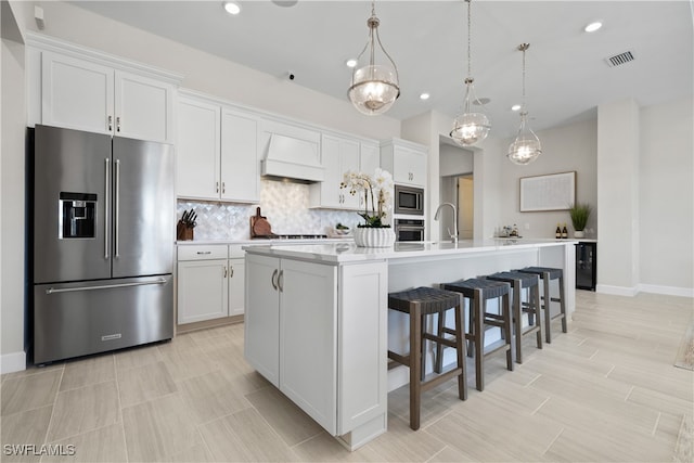 kitchen featuring pendant lighting, stainless steel appliances, white cabinetry, and a kitchen island with sink