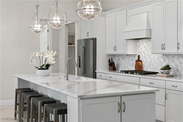 kitchen featuring backsplash, an island with sink, white cabinets, custom exhaust hood, and appliances with stainless steel finishes