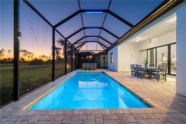 pool at dusk featuring glass enclosure, a patio, and a hot tub