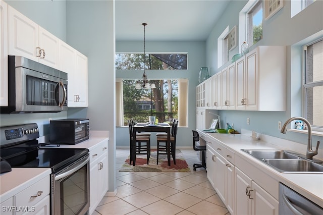 kitchen with light tile patterned flooring, appliances with stainless steel finishes, hanging light fixtures, sink, and white cabinets