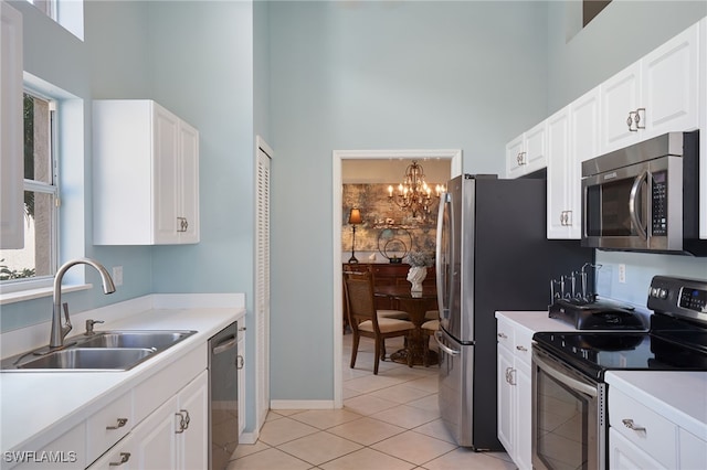 kitchen with a towering ceiling, stainless steel appliances, white cabinetry, an inviting chandelier, and sink