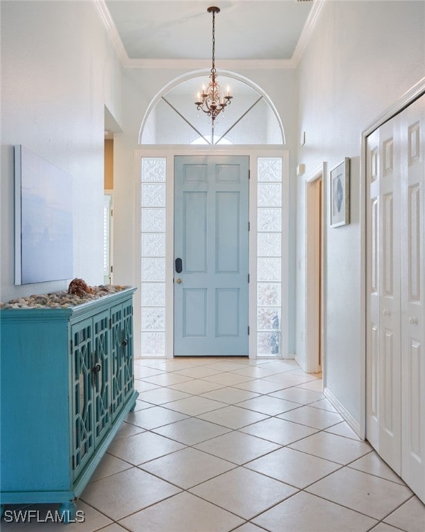 tiled foyer with ornamental molding, a notable chandelier, and a high ceiling