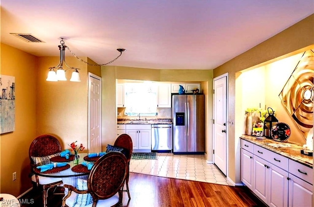 kitchen with white cabinetry, appliances with stainless steel finishes, light stone countertops, decorative light fixtures, and light wood-type flooring