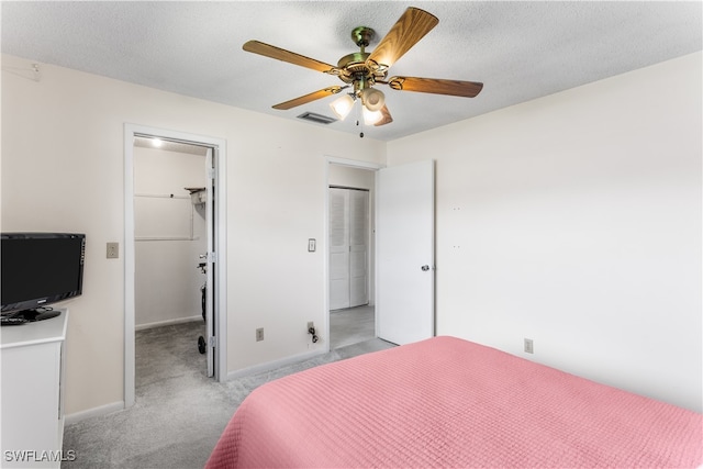 bedroom with a textured ceiling, light carpet, ceiling fan, a closet, and a walk in closet