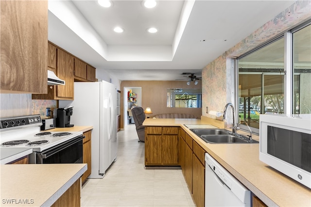 kitchen with a raised ceiling, decorative backsplash, sink, white appliances, and ceiling fan