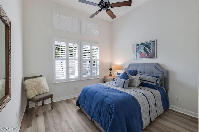 bedroom featuring ceiling fan, a towering ceiling, and light wood-type flooring