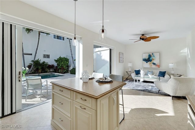 kitchen featuring light tile patterned floors, a breakfast bar, hanging light fixtures, cream cabinets, and a kitchen island