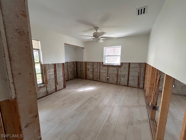 empty room with ceiling fan, light wood-type flooring, and tile walls