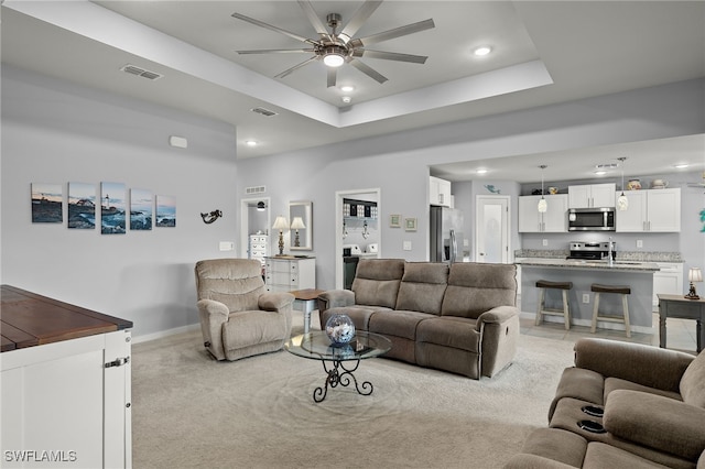 living room with light carpet, ceiling fan, and a tray ceiling