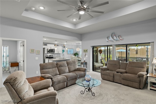 living room with sink, light colored carpet, ceiling fan, and a raised ceiling