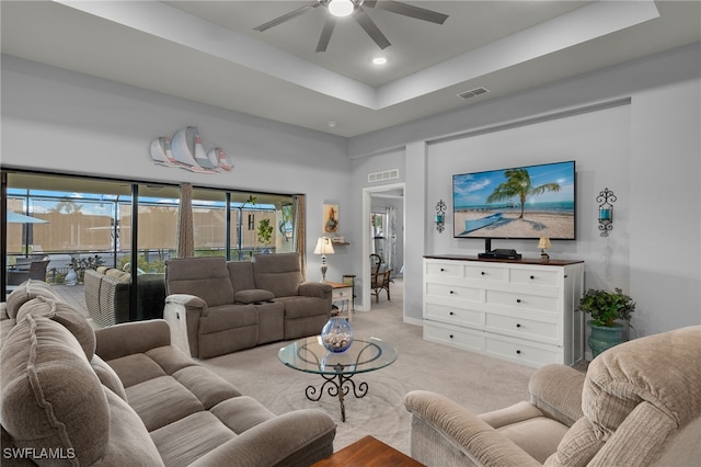 living room with a tray ceiling, light carpet, and ceiling fan