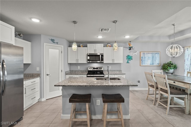 kitchen featuring white cabinets, appliances with stainless steel finishes, an island with sink, and hanging light fixtures