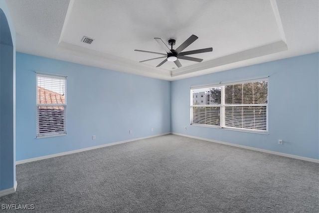 carpeted empty room with ceiling fan and a raised ceiling