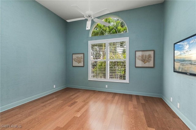 spare room with ceiling fan, plenty of natural light, wood finished floors, and baseboards