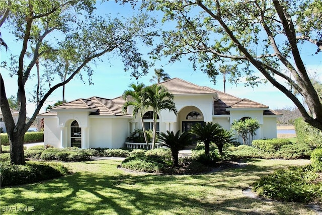 mediterranean / spanish-style house with a front yard, a tile roof, and stucco siding