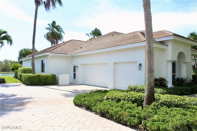 view of property exterior with a garage, decorative driveway, a tile roof, and stucco siding