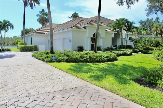 view of property exterior with decorative driveway, a tile roof, a yard, stucco siding, and an attached garage